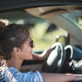 Una mujer conduce con confianza un automóvil con su esposo sentado a su lado, ambos concentrados en el camino que tiene por delante.