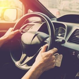 Un hombre conduciendo un automóvil con el sol brillando en el fondo, creando una vista panorámica en la carretera.