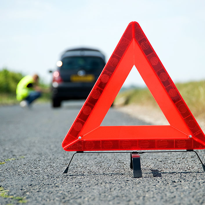 Una señal de advertencia de triángulo rojo a la costada de la carretera que indica peligros potenciales más adelante.