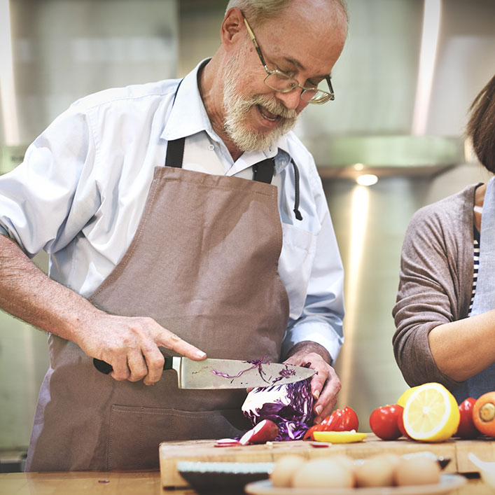 Una pareja de ancianos cocinando alegremente juntos en su cocina, creando una deliciosa comida con amor y cuidado.