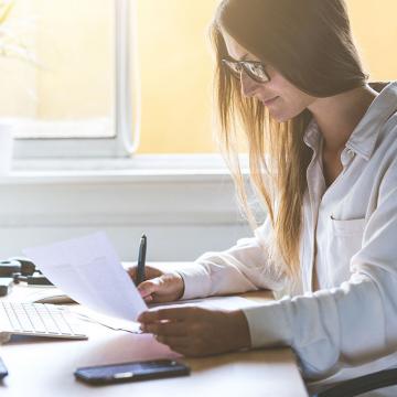 Una mujer que trabaja en un escritorio con una computadora portátil y papeles, concentrada en sus tareas.