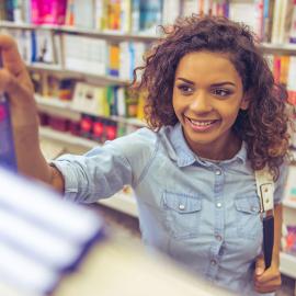 Una mujer absorta en un libro en una biblioteca, rodeada de estanterías llenas de conocimiento.